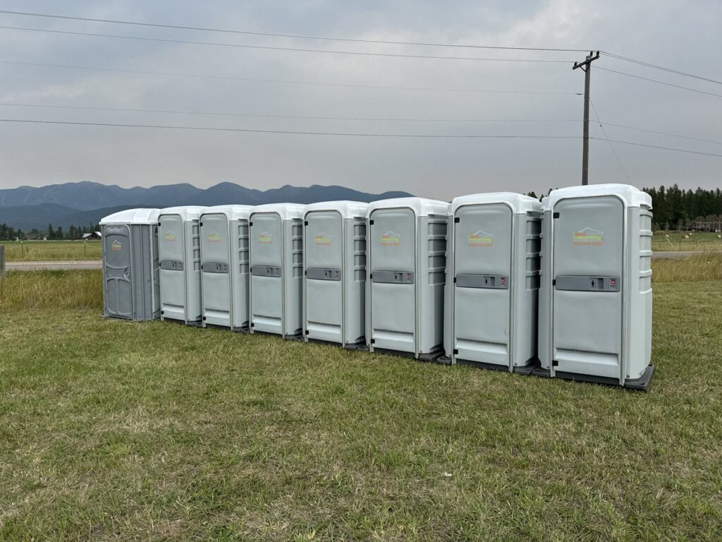 Row of clean portable restrooms on a grass lot with mountains in the background